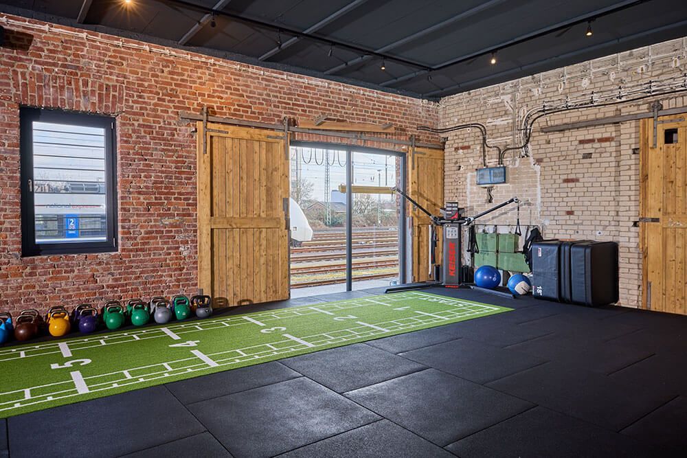 Ein Fitnessraum mit einem grünen Kunstrasenfeld, ausgestattet für verschiedene Sport- und Trainingsaktivitäten.