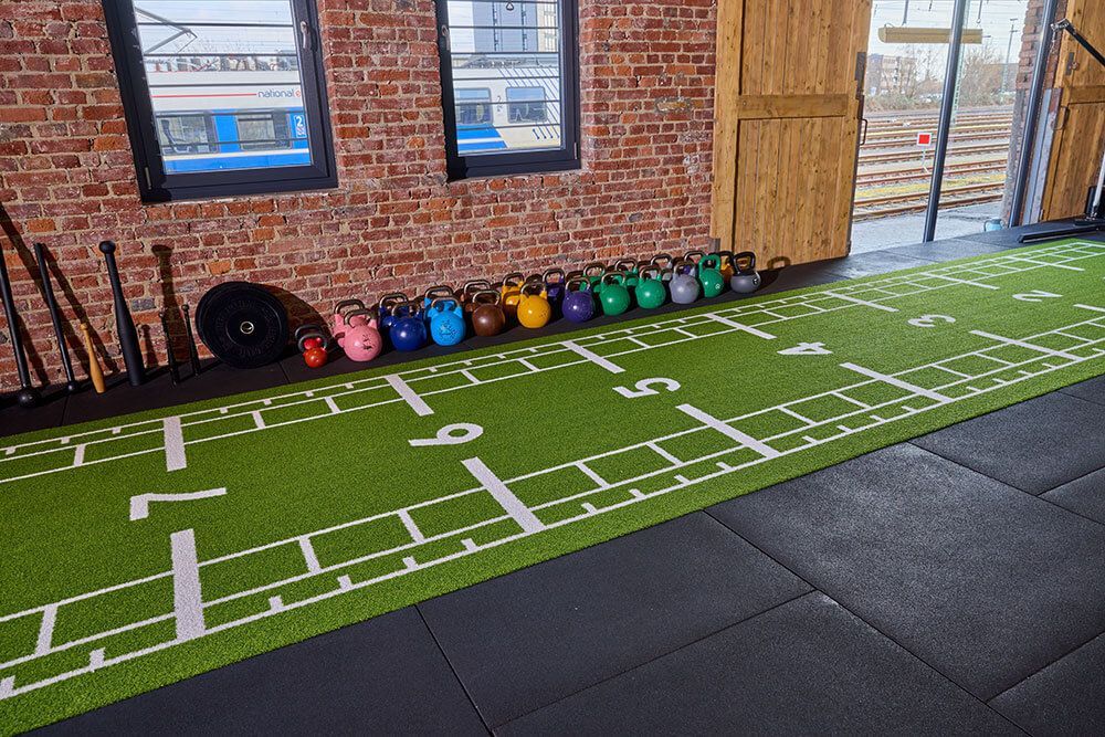 Ein Fitnessraum mit einem grünen Kunstrasenfeld, ausgestattet für verschiedene Sport- und Trainingsaktivitäten.