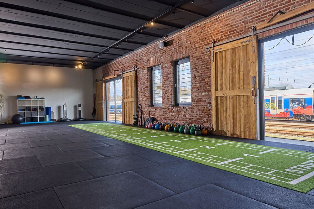 Ein Fitnessraum mit einem grünen Kunstrasenfeld, ausgestattet für verschiedene Sport- und Trainingsaktivitäten.